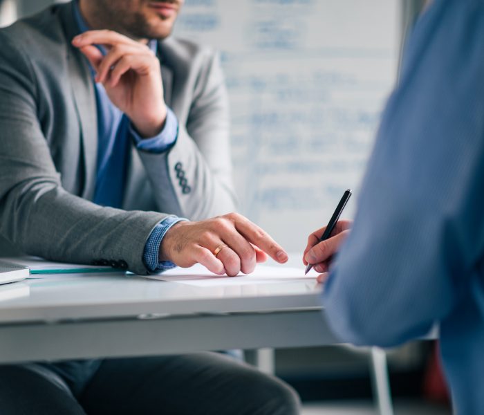 Low angle image of two men in formal wear sitting at the desk and and signing agreement.